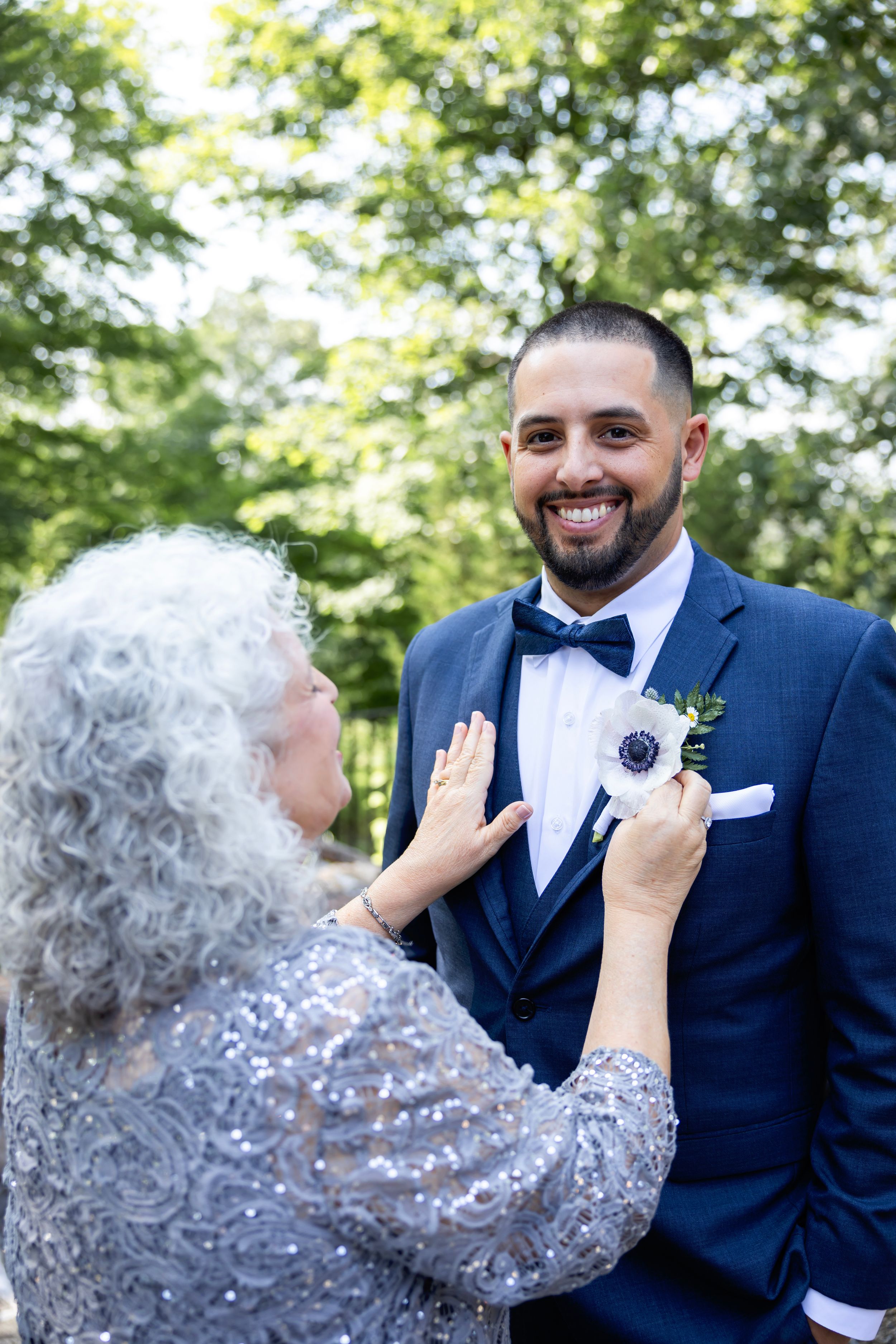 A sweet moment showing a groom having his bowtie adjusted at an outdoor wedding ceremony.