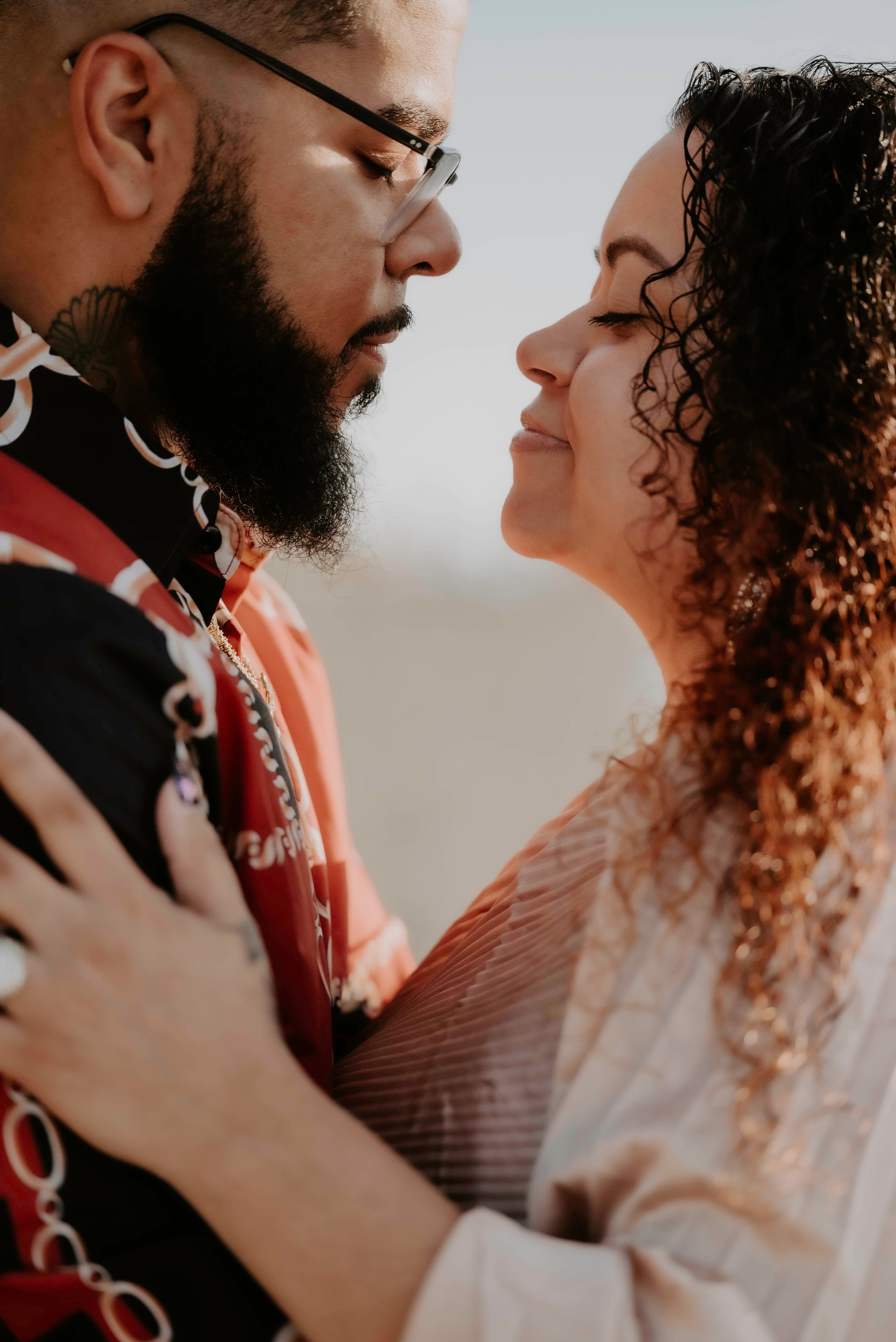 A bearded man with glasses and a woman with curly hair share a romantic close moment, facing each other tenderly.