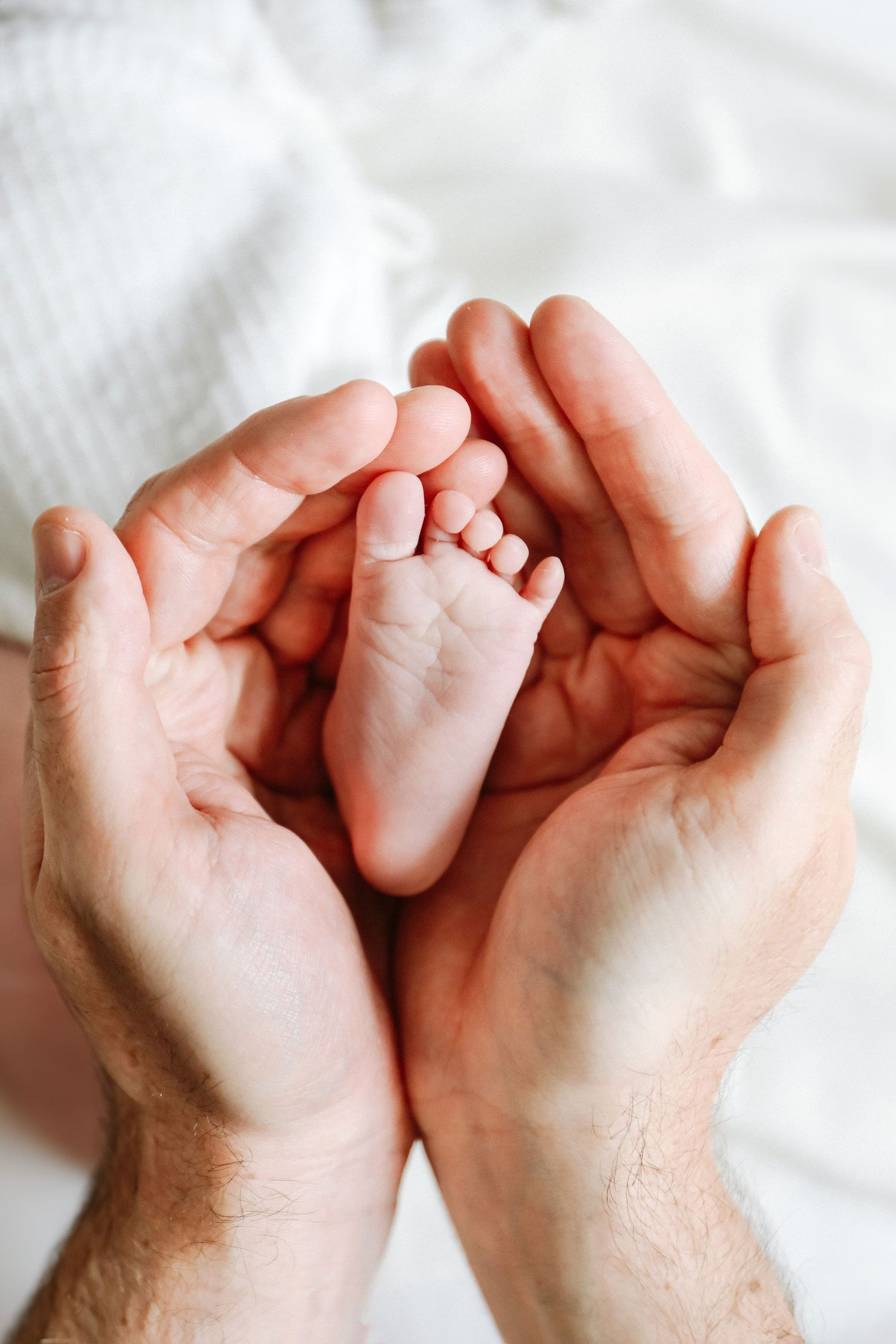 Adult hands gently cradle a tiny baby foot, capturing a tender parenting moment, during newborn photoshoot in Nottingham