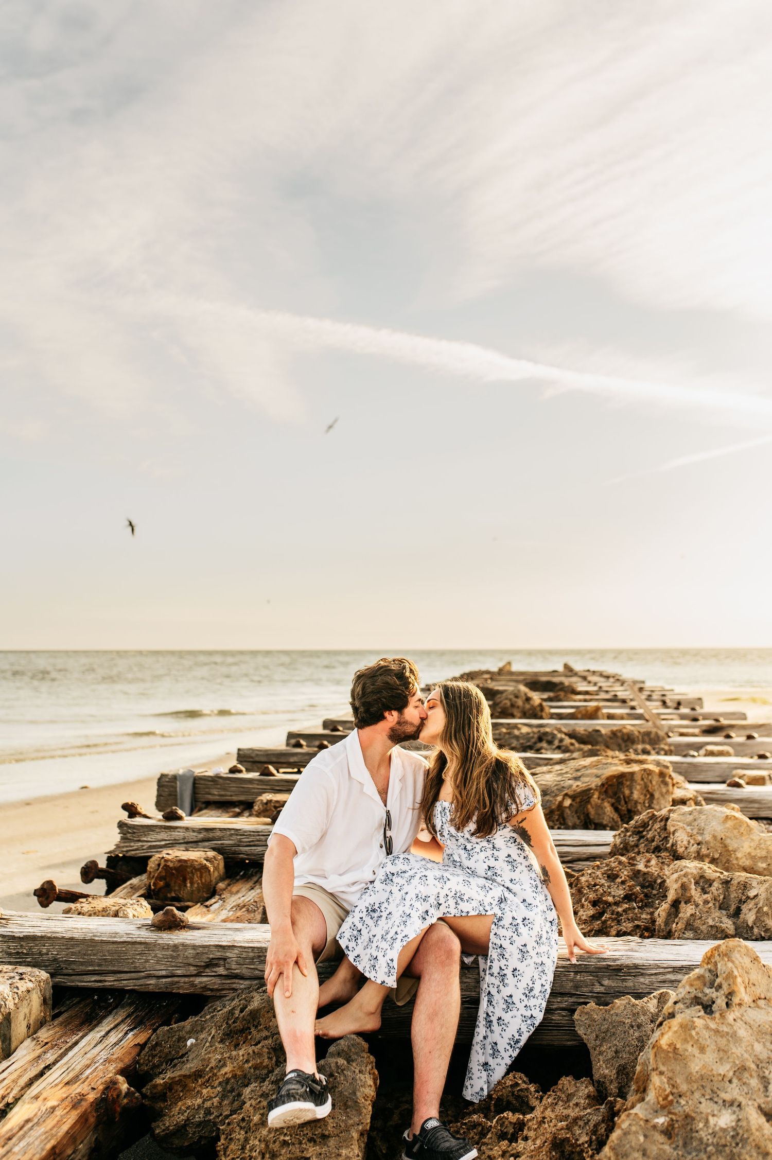 Intimate couple sharing romantic moment on wooden jetty by ocean at sunset.