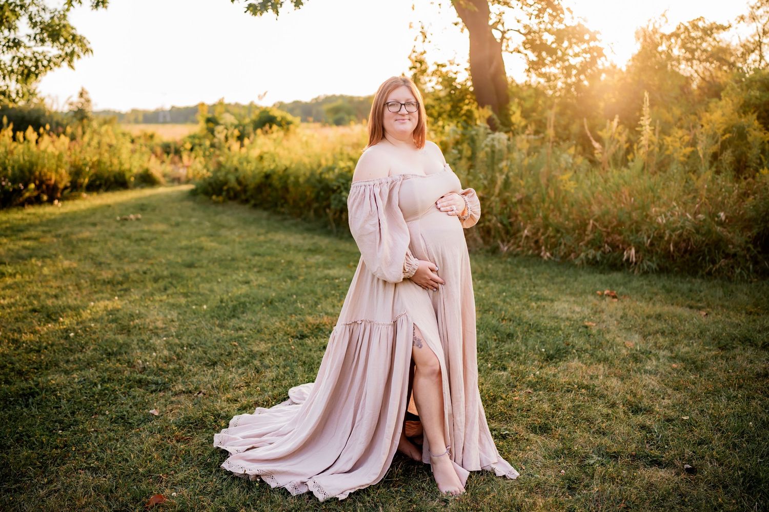 A person in a flowy pink dress stands in a sunlit meadow during golden hour.