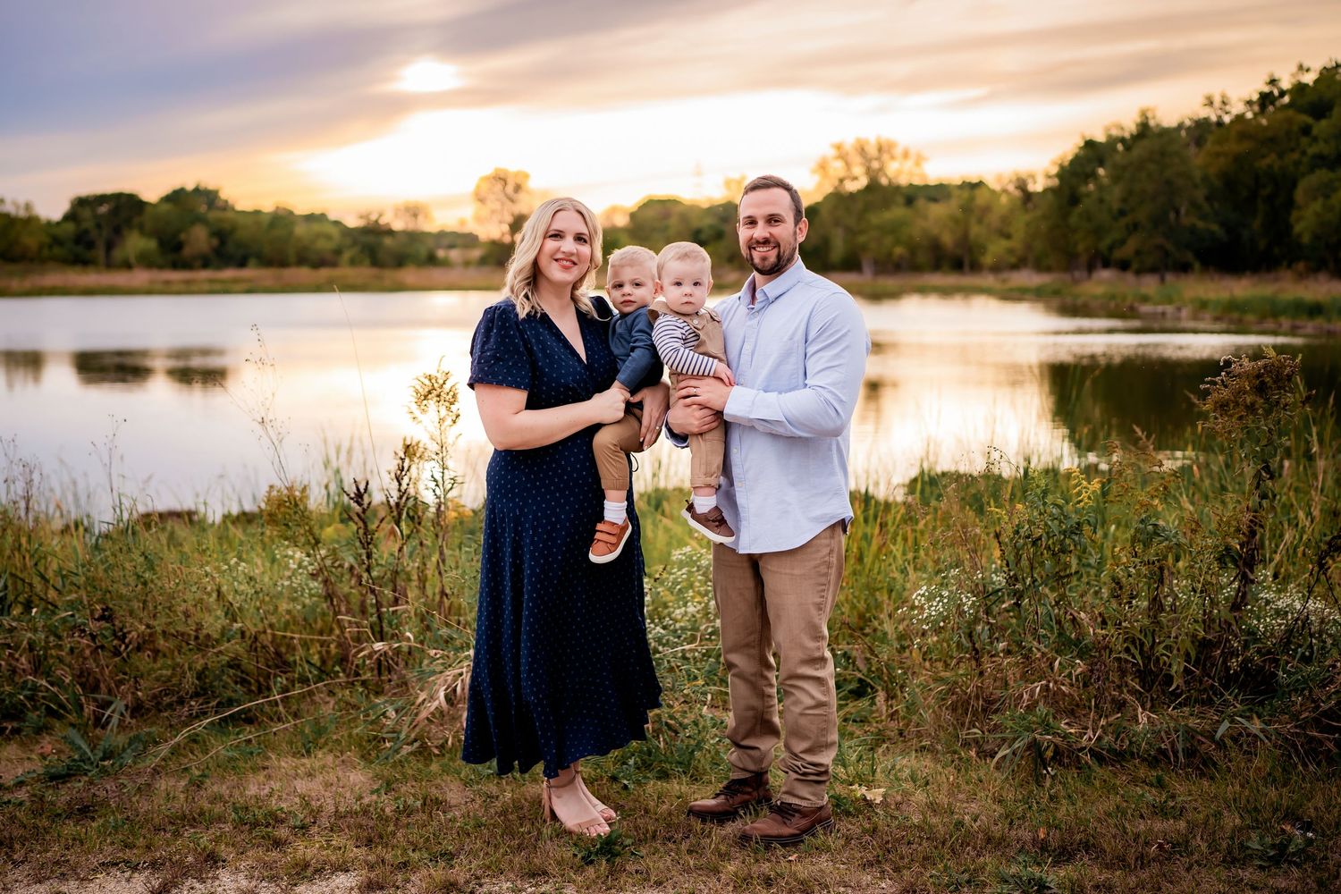 Happy family enjoys sunset photoshoot by peaceful lake surrounded by wildflowers and natural beauty.