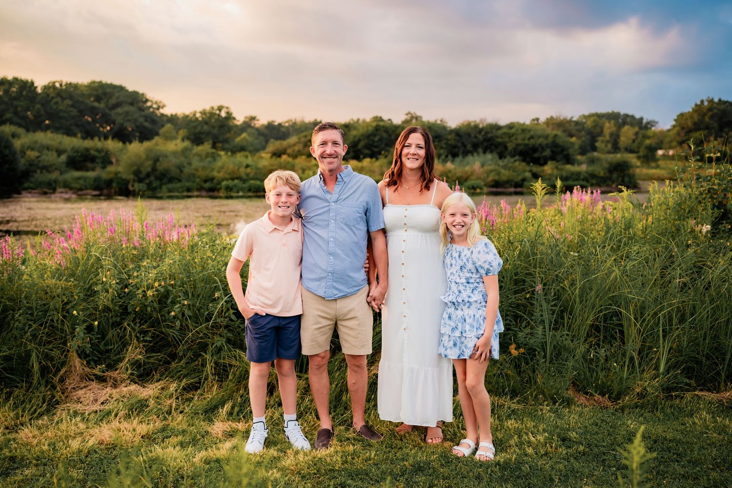 Family standing together in a field of wildflowers at sunset with trees in the background.