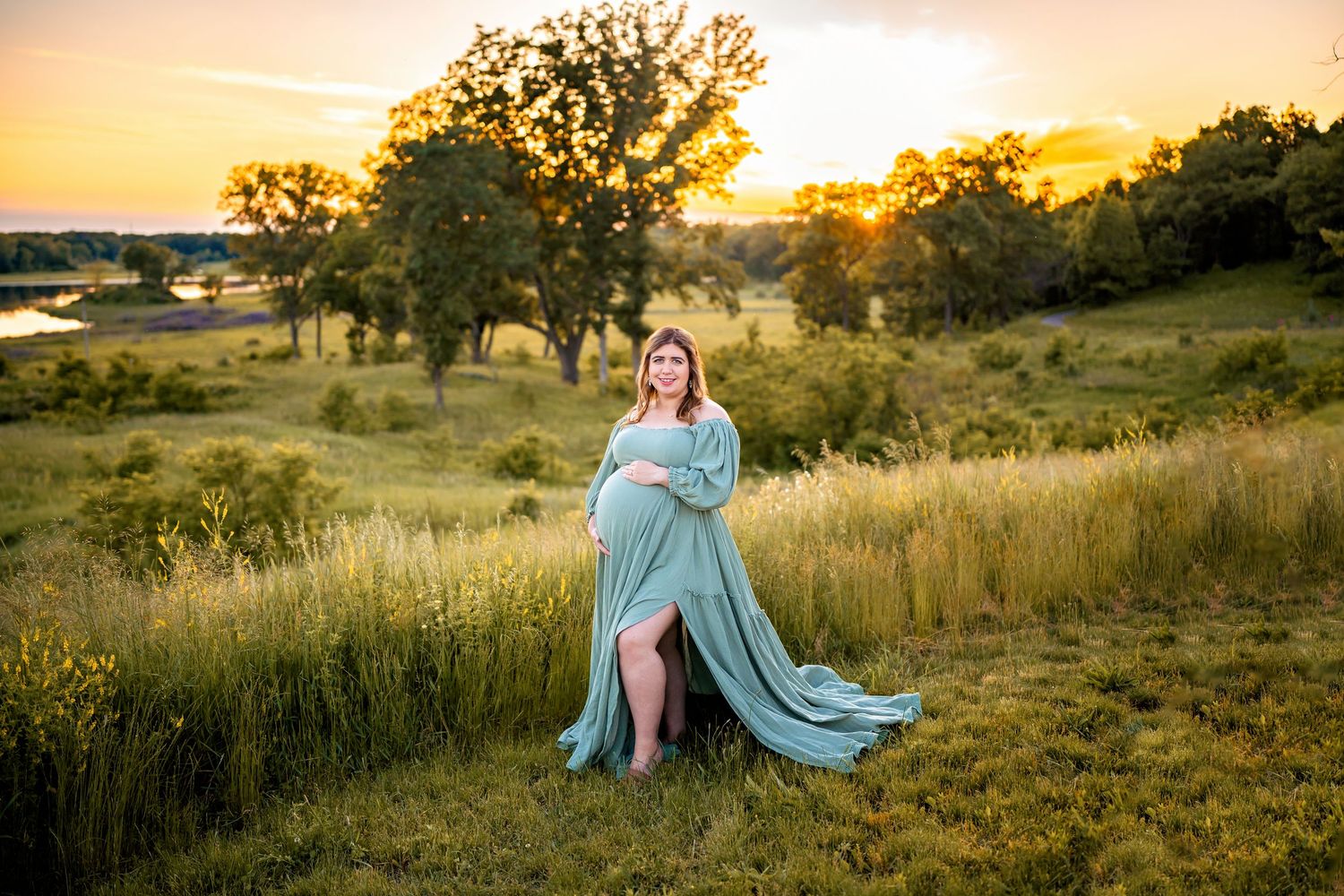 Silhouetted against the warm glow of sunset, figures sit in a hillside meadow amongst tall grass and scattered trees.