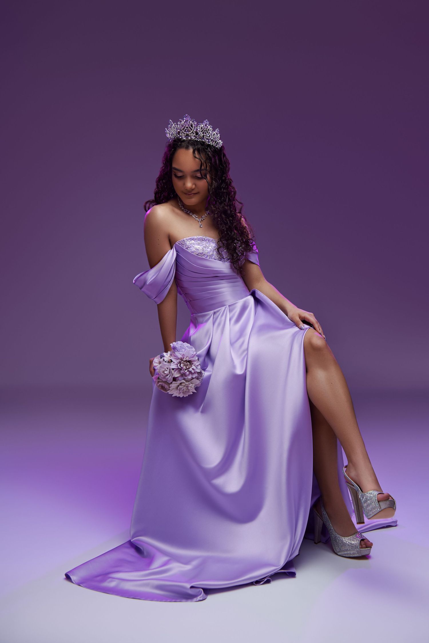 Elegant lilac satin gown with silver crown and matching bouquet on purple backdrop during glamorous photoshoot. nj photographer