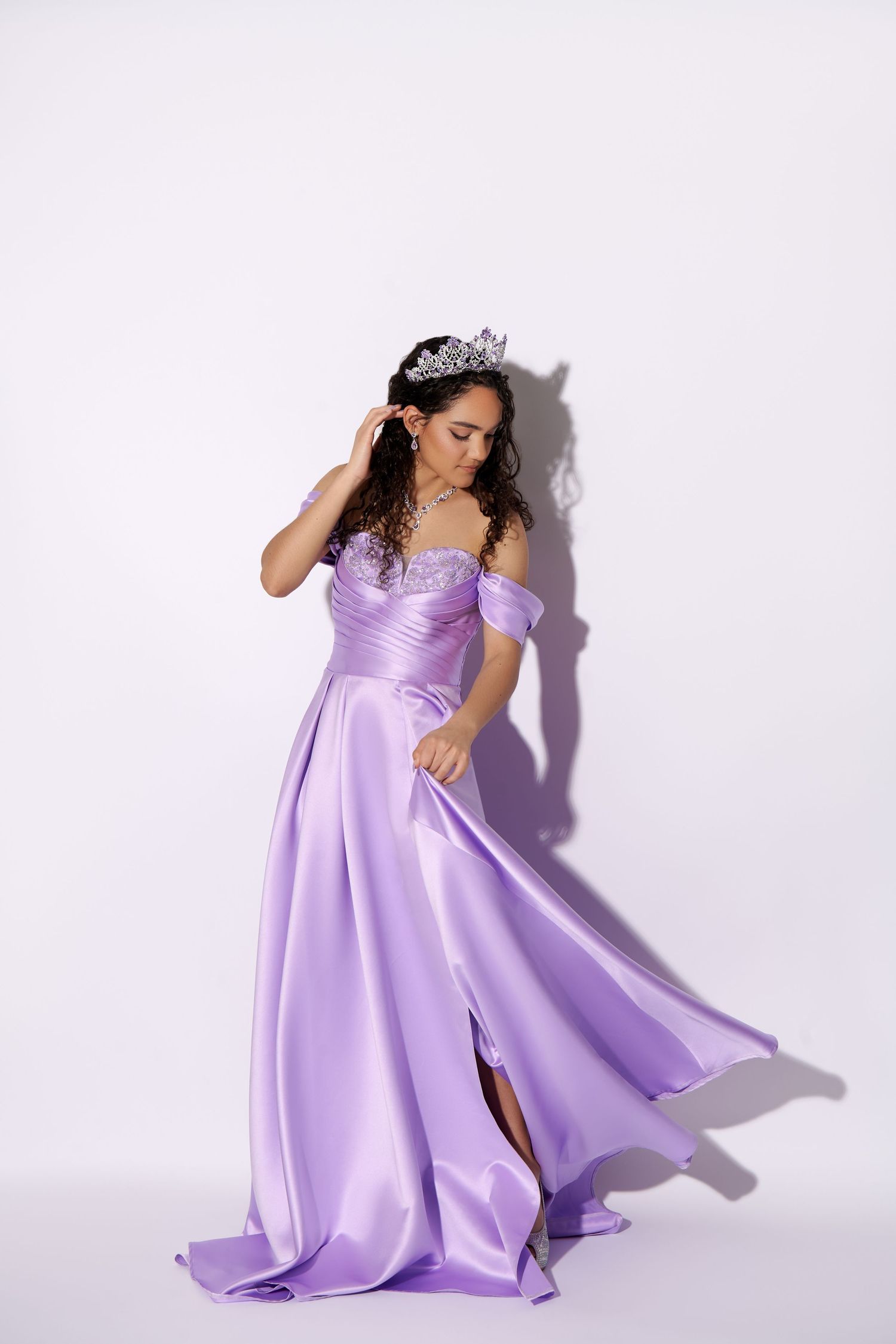 A person in a flowing lavender ball gown and tiara twirls against a white backdrop, creating elegant movement.