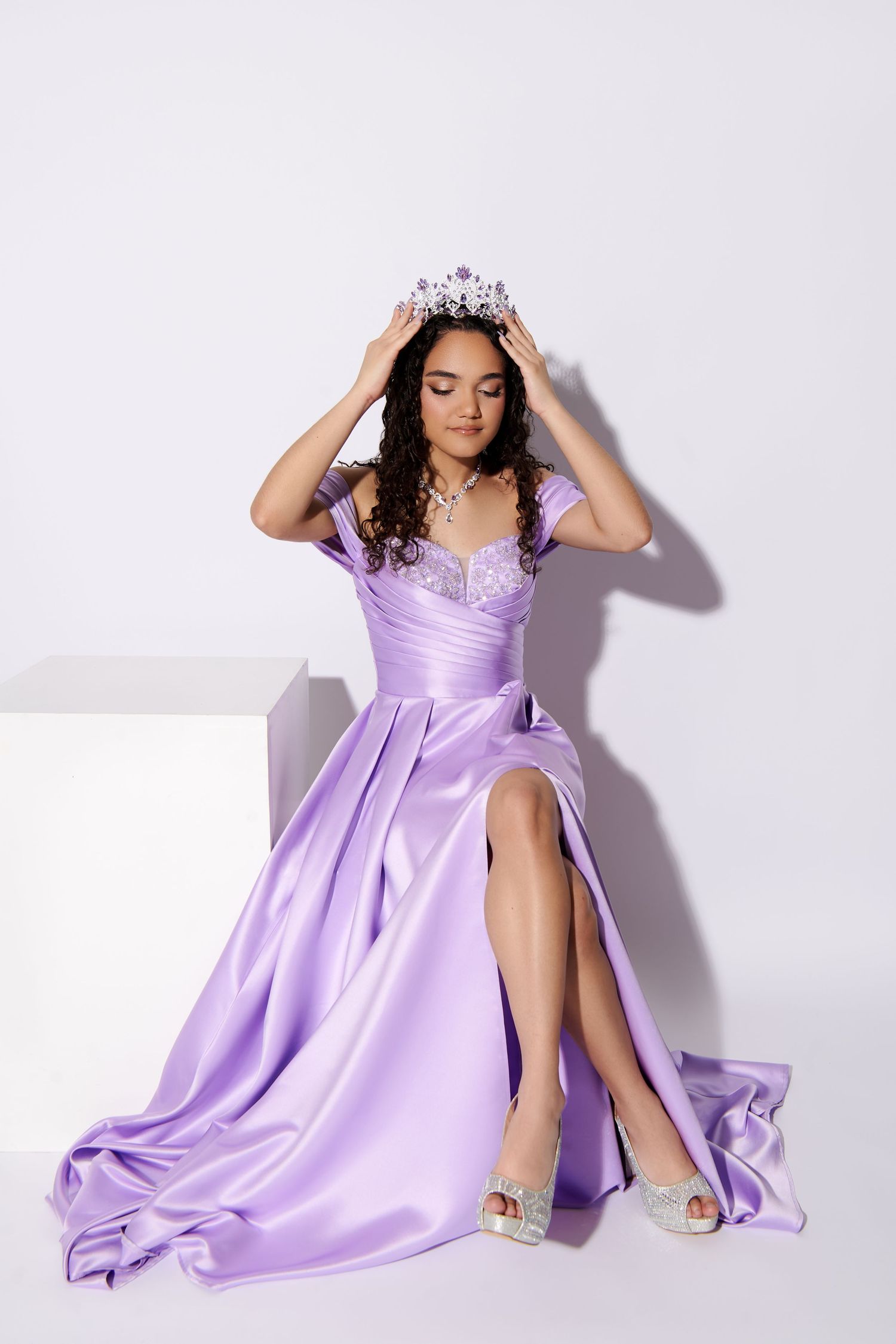A person in a flowing lilac gown and silver crown poses gracefully against a white background. sweet sixteen portraits nj