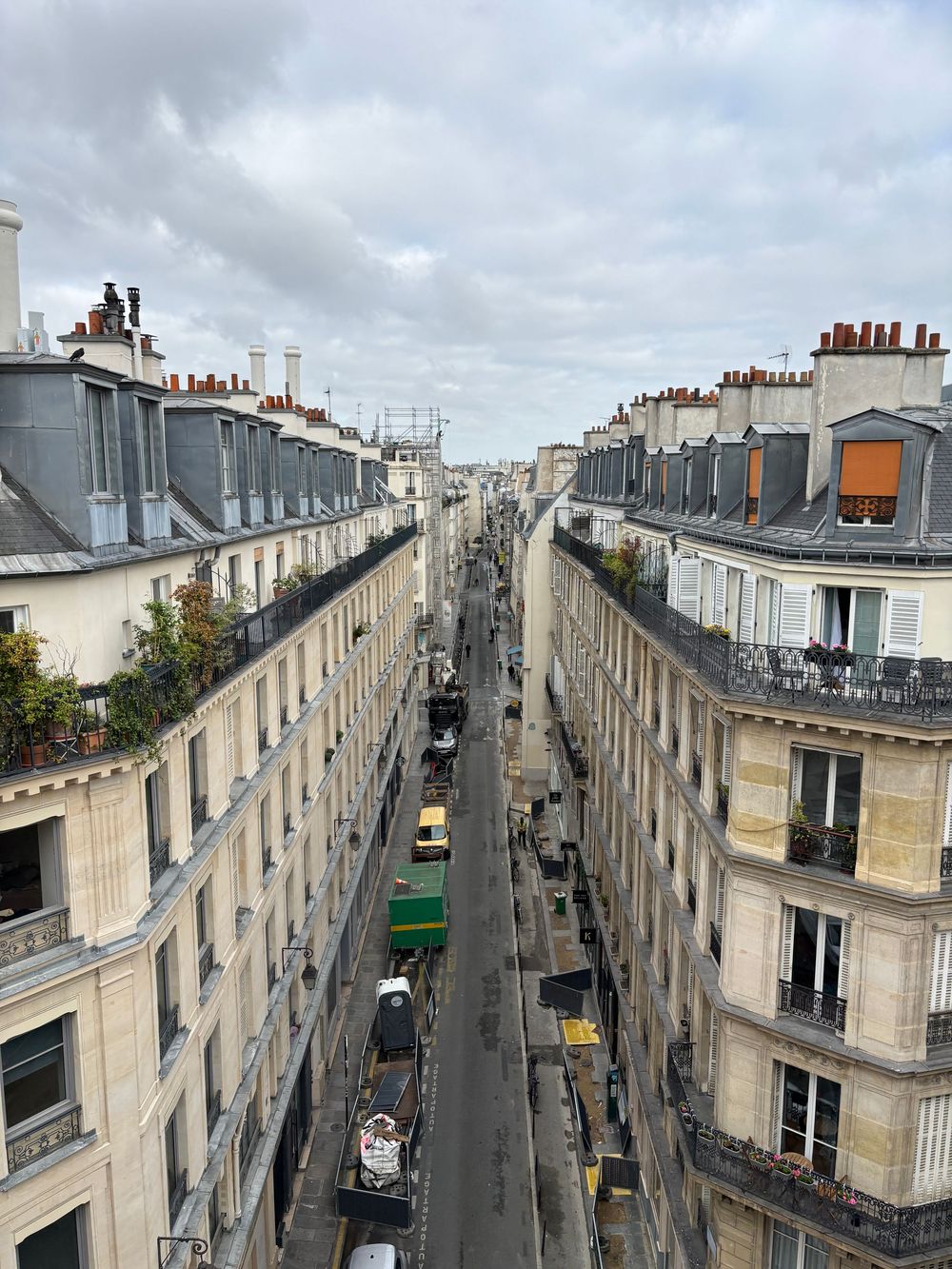 View down a narrow Parisian street lined with traditional Haussmann-style apartment buildings and parked cars.
