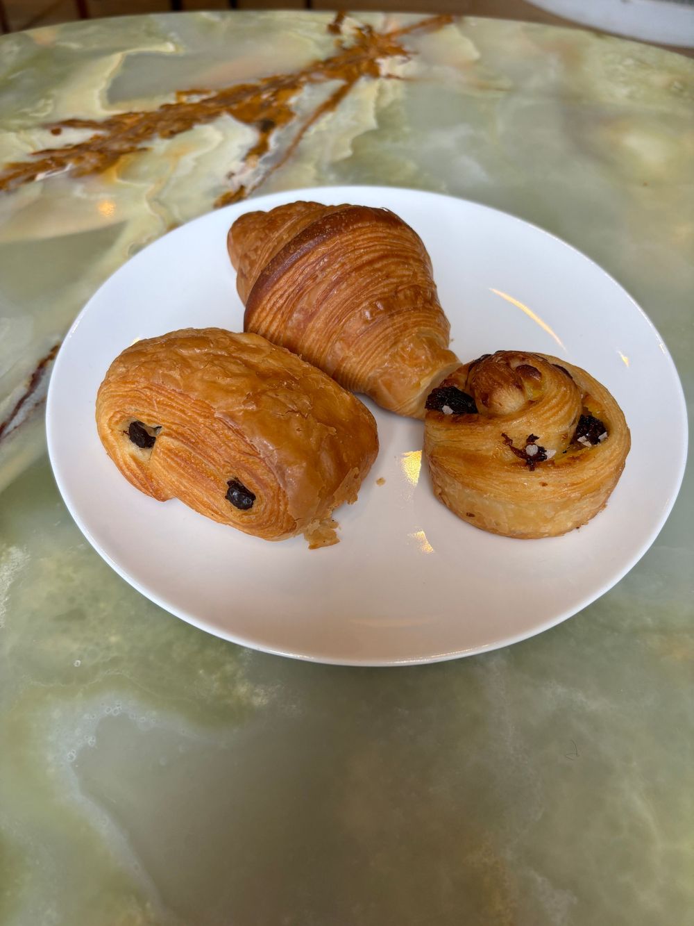 Two chocolate-filled croissants served on a simple white plate against a muted green surface.