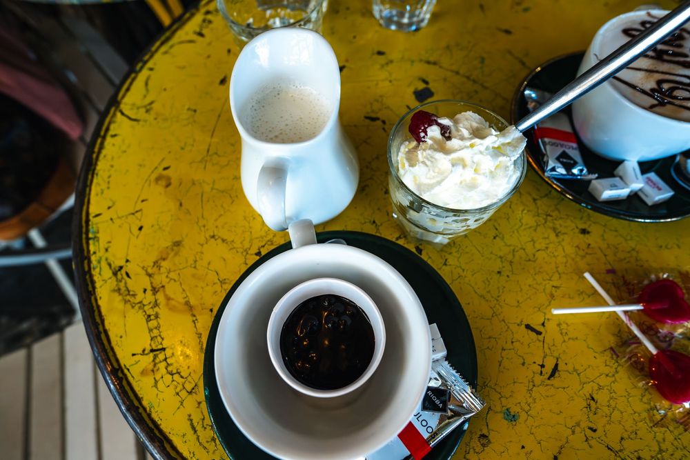 Overhead view of black coffee in a ceramic cup with cream and sugar on a distressed yellow table surface.