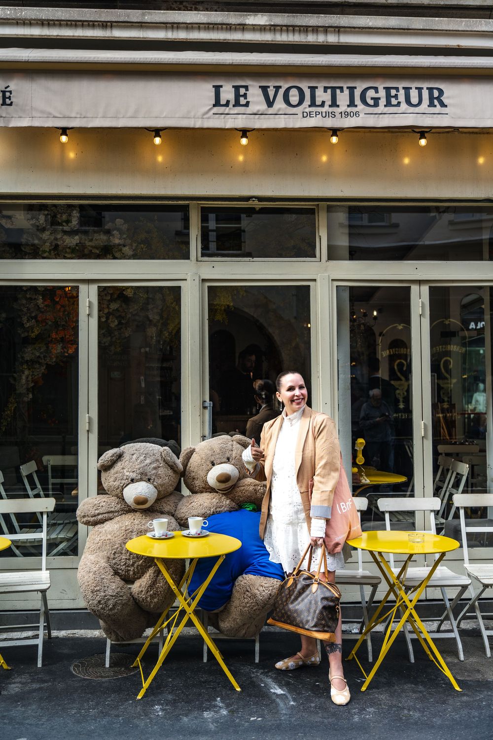 Le Voltigeur cafe in Paris with two large teddy bears at yellow outdoor tables and casual chic street style.