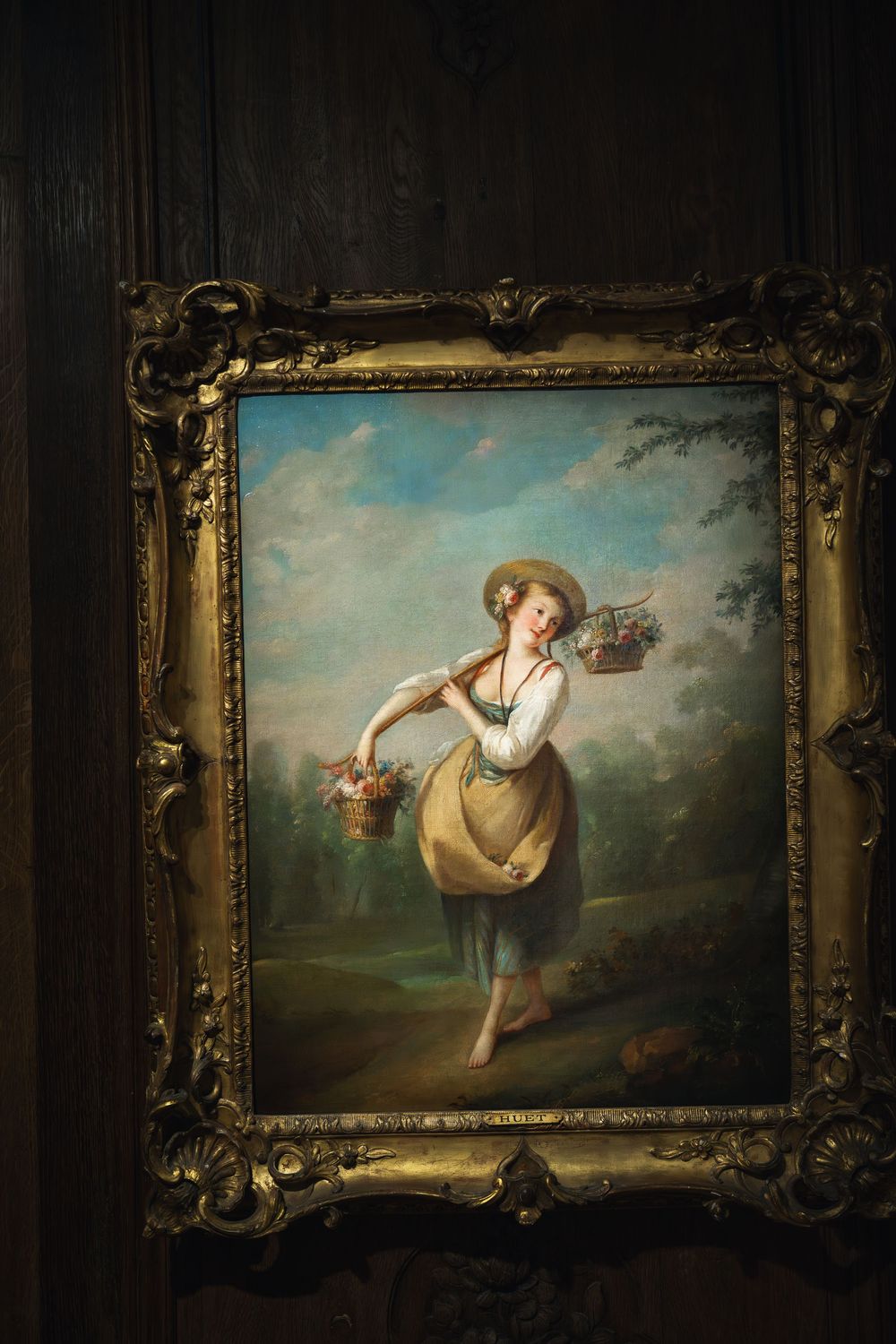 Classical painting in ornate gold frame shows a dancing woman in white dress carrying baskets of flowers in a pastoral scene.