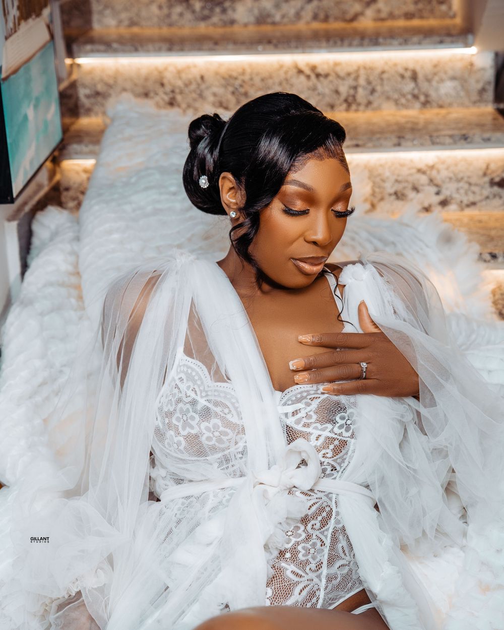 Bride in dreamy white lace lingerie and tulle robe poses on marble steps.