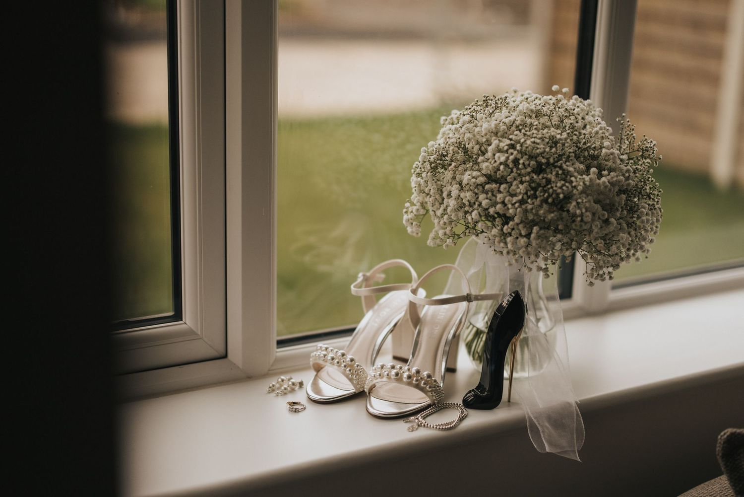 White babys breath flowers and elegant wedding shoes sit on a window ledge in soft natural lighting.
