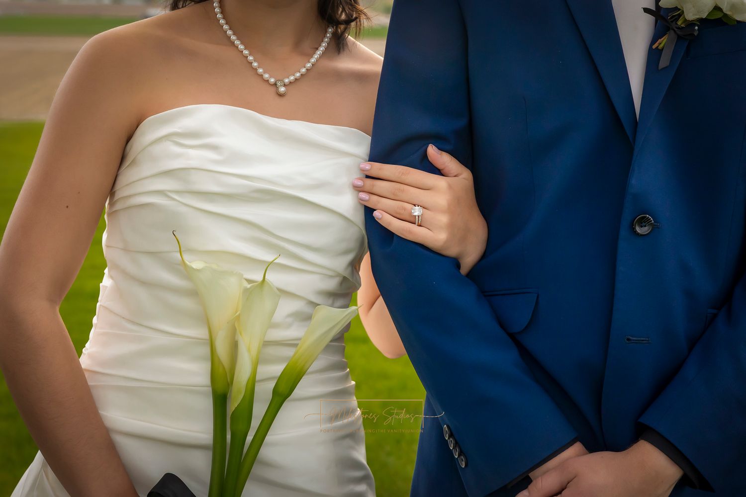 focus on wedding ring on bride's finger while holding groom's arm, bride holding calla lilies