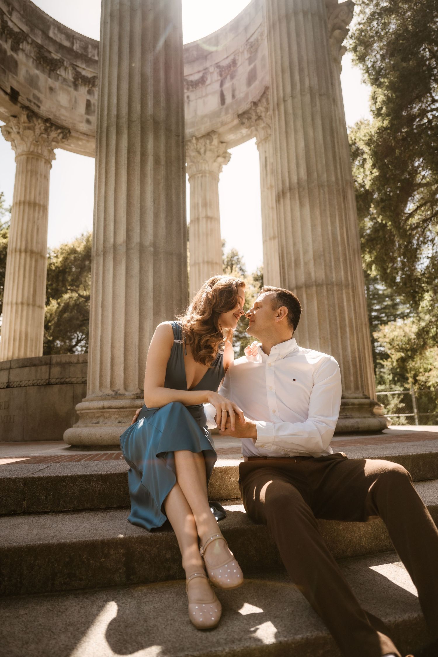 Romantic couple lounging by classical stone columns at sunset.