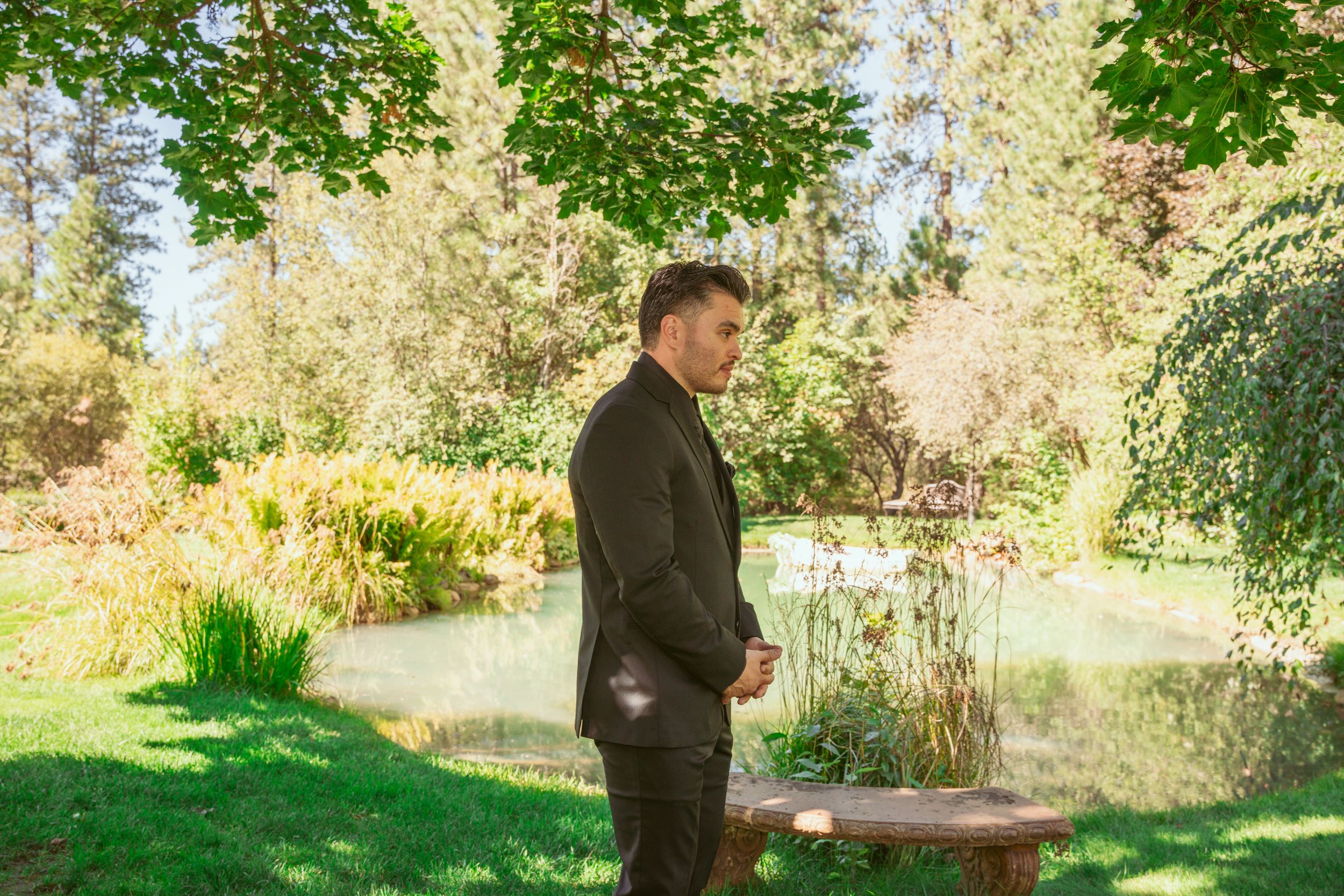 A couple stands in a lush green garden setting during what appears to be an outdoor photography session.