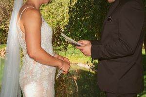 A couple in wedding attire joins hands during an outdoor garden ceremony celebration.