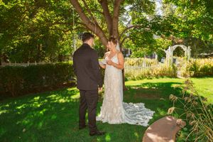 A couple shares a special moment in a sunlit garden with a white arbor and lush greenery in the background.