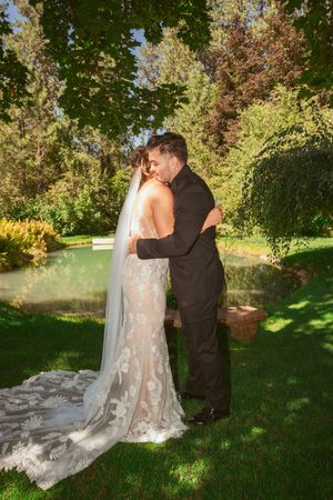 A couple embraces in a romantic moment during their outdoor garden wedding against a backdrop of lush greenery.