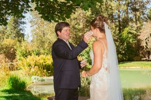 A couple shares a tender moment by a pond in a lush garden setting during their wedding ceremony.