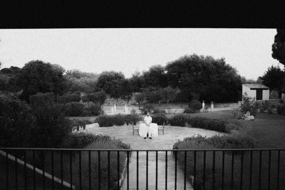 A black and white view from a balcony overlooking people gathered in a garden courtyard with trees and buildings.