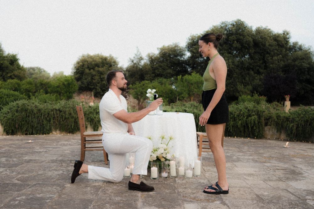 A couple enjoys a romantic sunset photo session on a rocky hill overlooking a lush landscape.