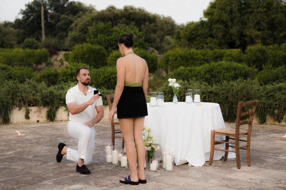 A couple sits on a stone wall overlooking a scenic garden during an intimate engagement photo session.