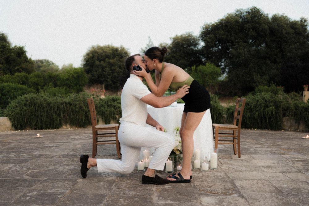 A couple in wedding attire embraces while sitting on stone steps in an outdoor setting.