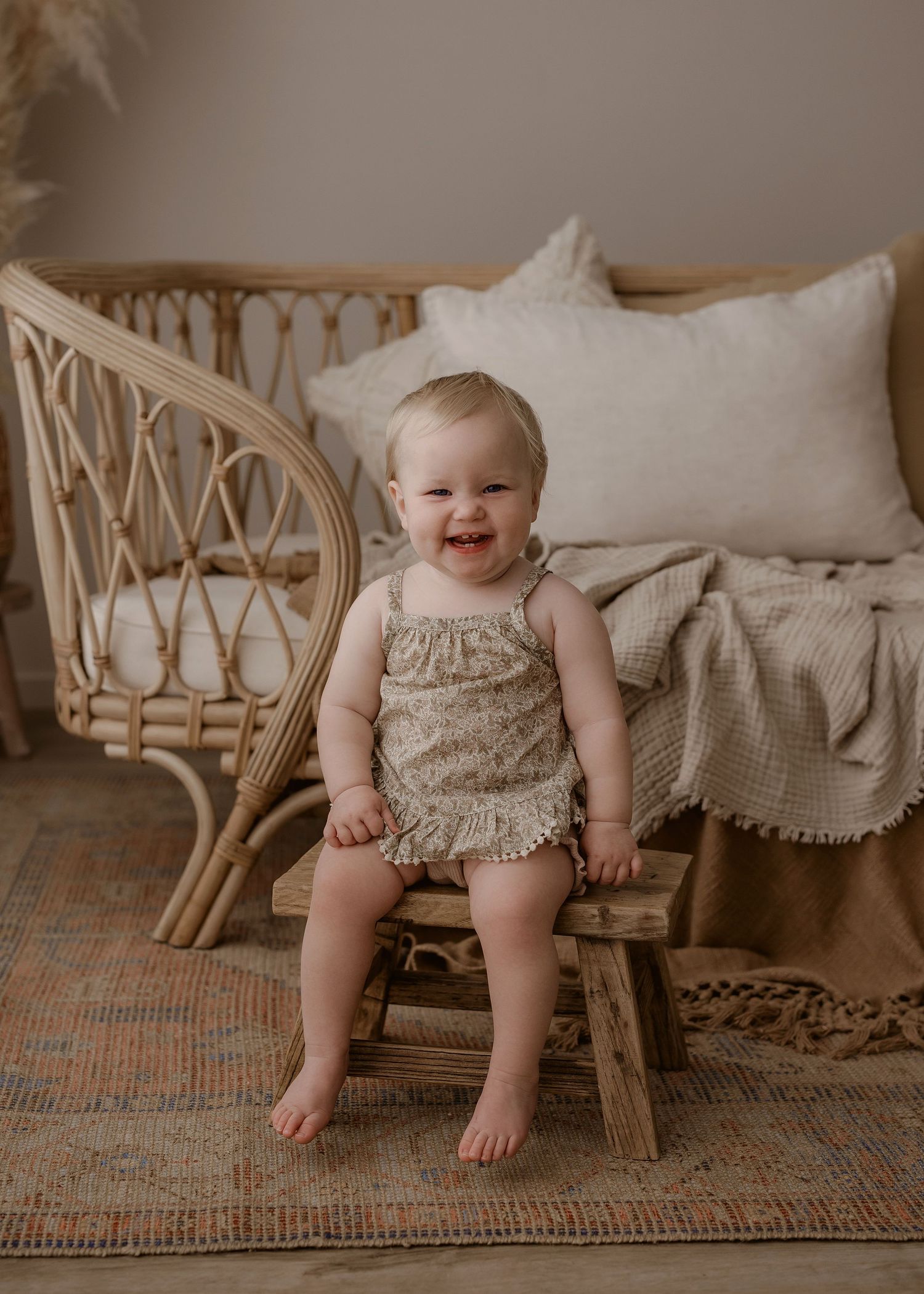 A young child sits on a vintage woven chair with cream-colored cushions on a patterned area rug. Photographed in a studio located in Papamoa