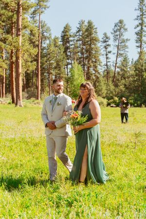 People celebrating a wedding ceremony in a sunny mountain meadow surrounded by tall pine trees in Colorado.