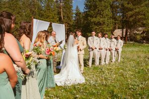 Wedding party stands in a scenic mountain meadow with wildflowers and pine trees in the background.