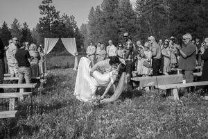 Black and white photo of wedding guests watching ceremony in rustic outdoor meadow setting.