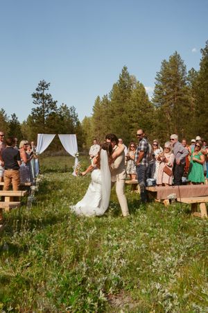 Wedding celebration in blooming meadow with guests seated on wooden benches under clear blue sky.
