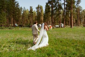 Couple dances together in a grassy meadow with tall pine trees creating a natural outdoor backdrop.