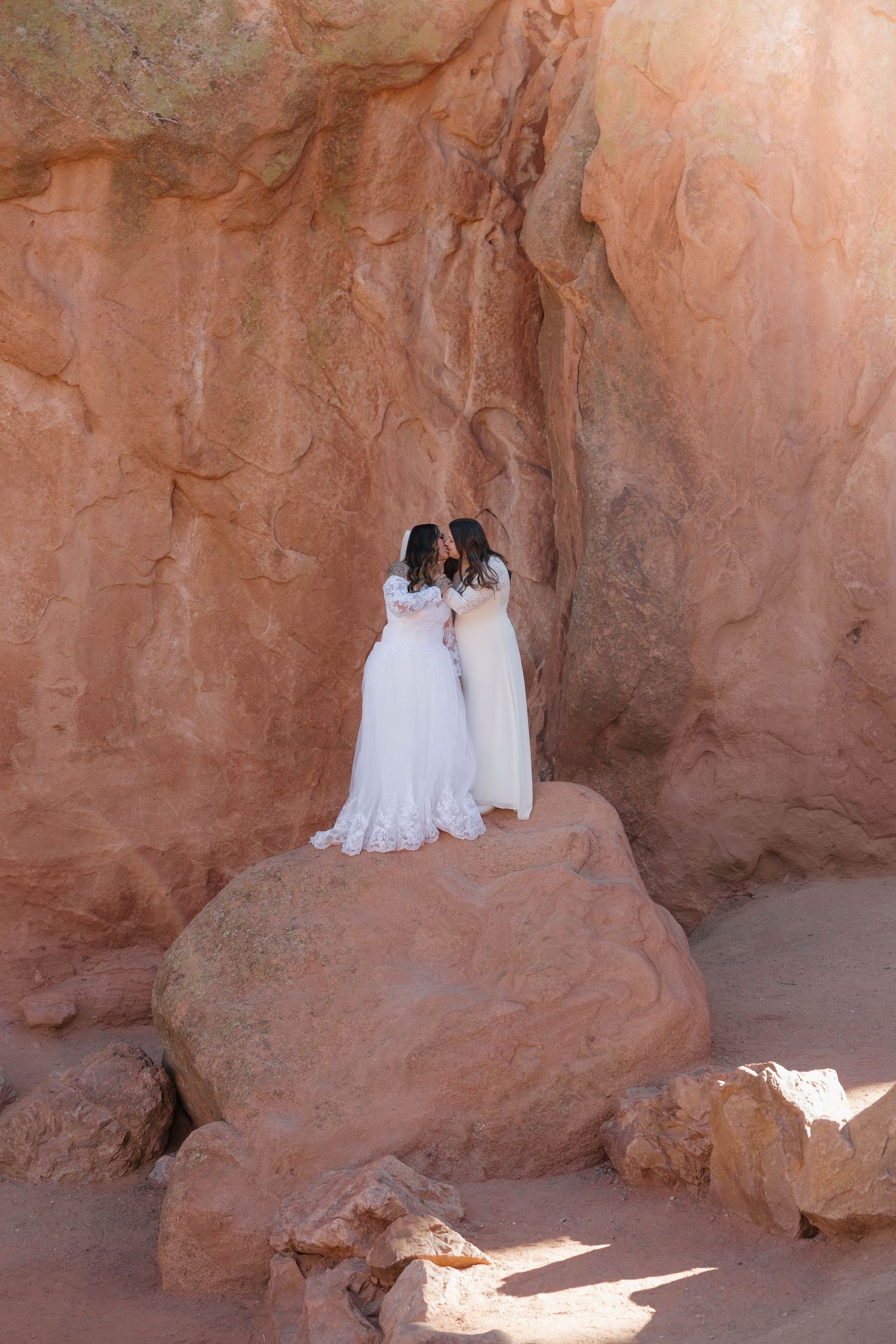 A romantic wedding photoshoot takes place among towering orange canyon walls in a natural desert setting.