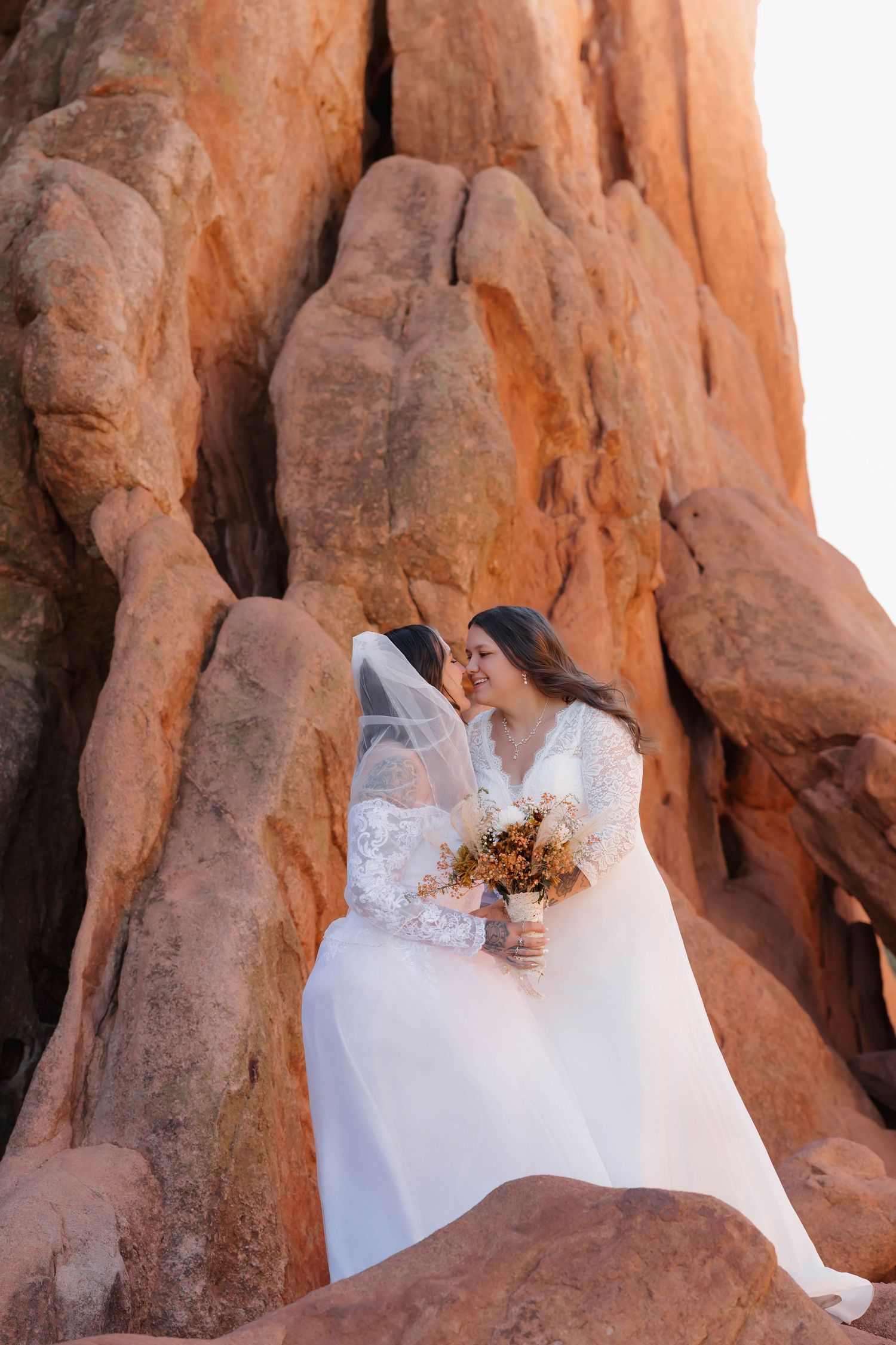 A couple in wedding attire embraces against stunning red rock formations in an outdoor desert landscape.