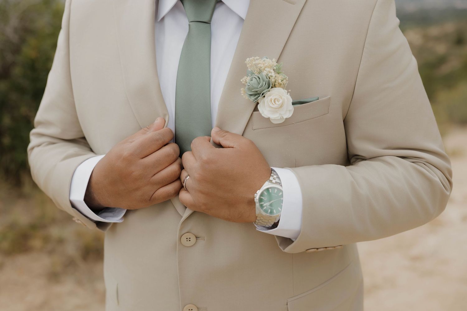 Close-up details of a beige suit with a light green tie and white boutonniere flower.
