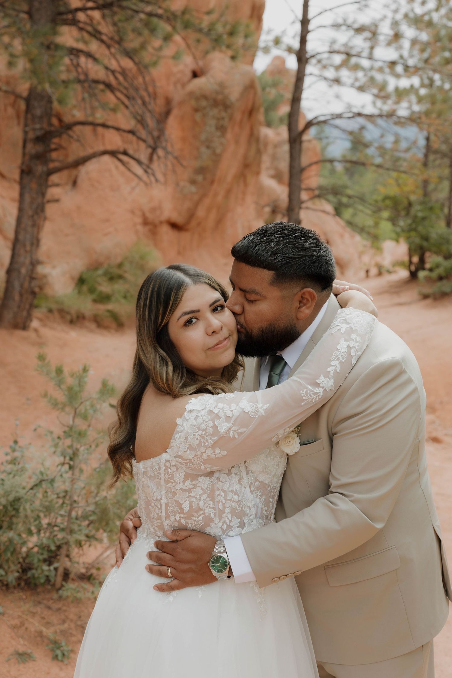 A romantic wedding couple embraces in front of red rock formations in a desert landscape during a photo session.