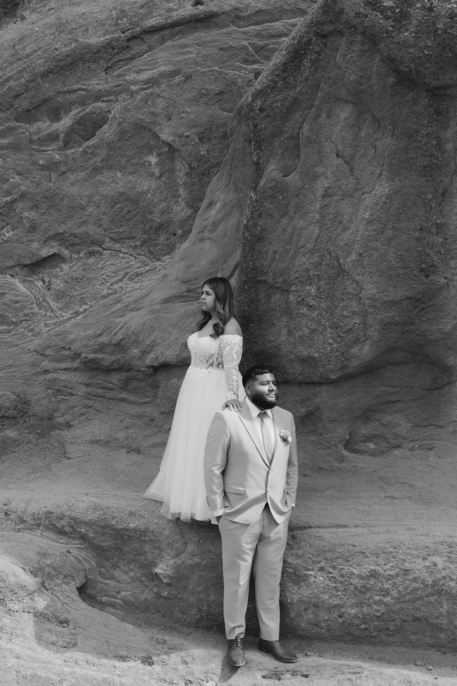 Wedding couple poses against dramatic red rock wall in elegant formal attire.