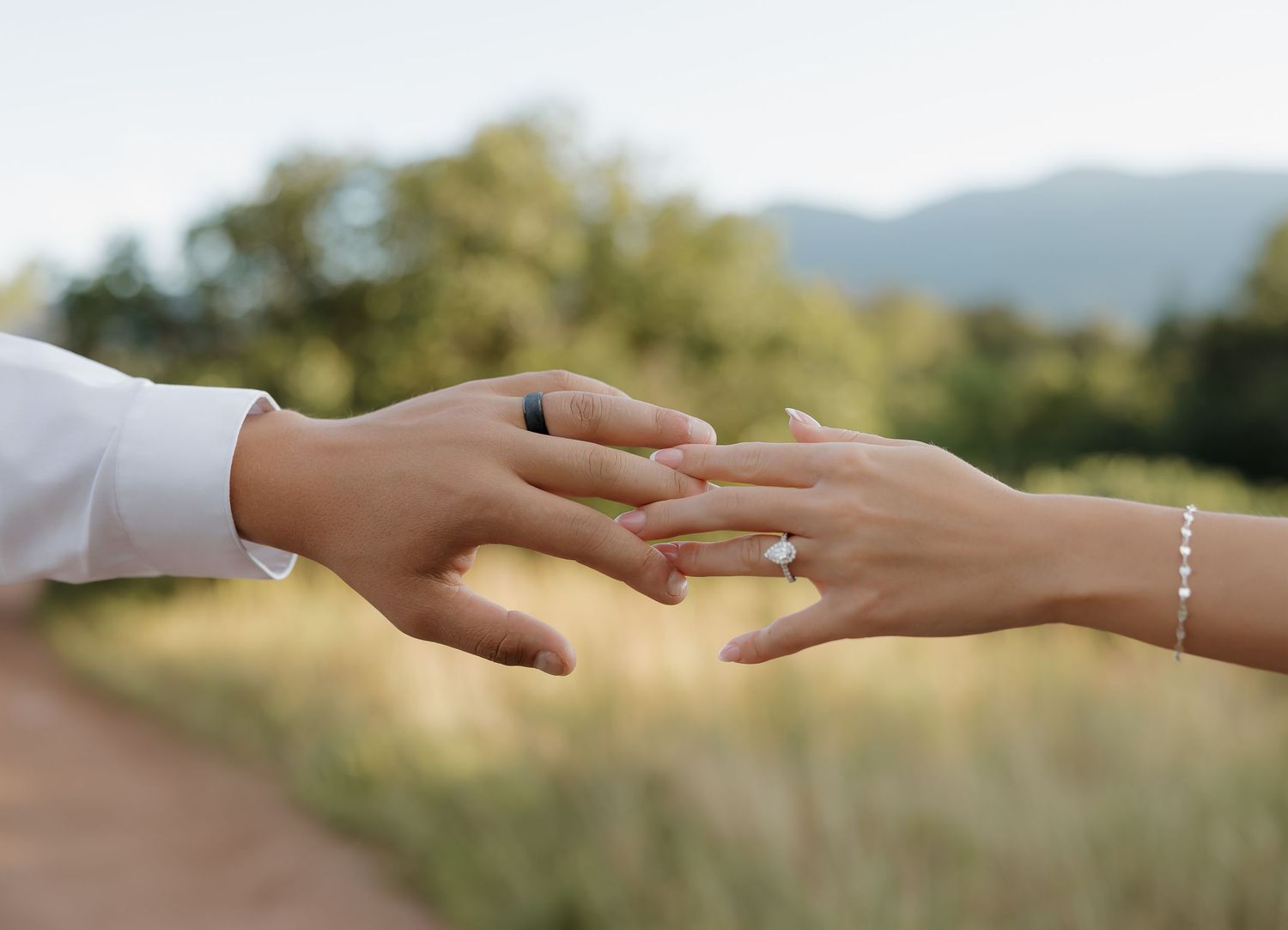 Two hands reaching towards each other with mountains and greenery in the background on a sunny day.