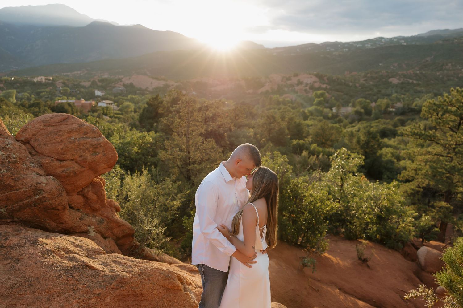Couple shares romantic sunset moment at Garden of the Gods park with red rock formations and mountain views in background.