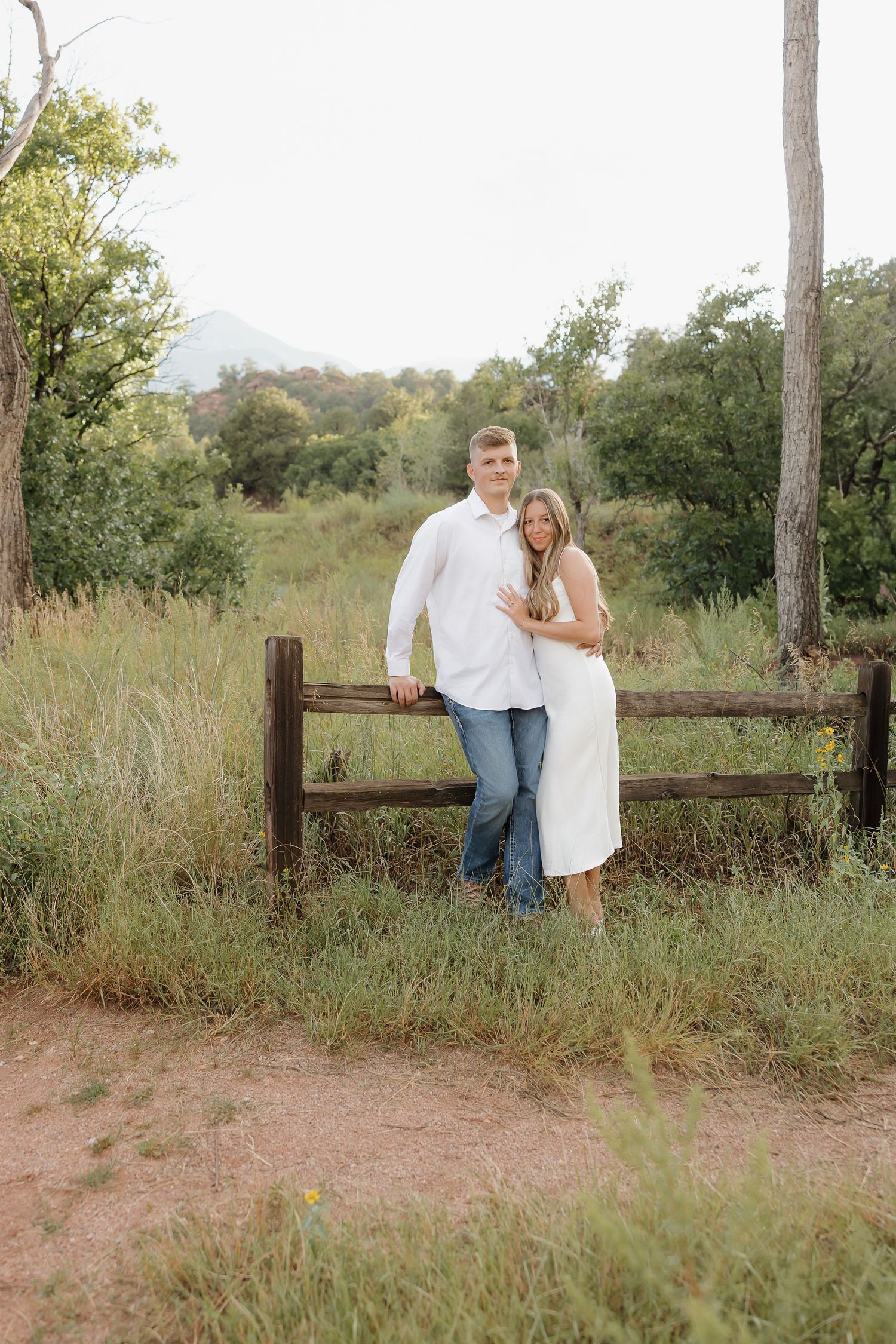 A couple shares romantic moments by a rustic wooden fence surrounded by tall grass and autumn foliage.