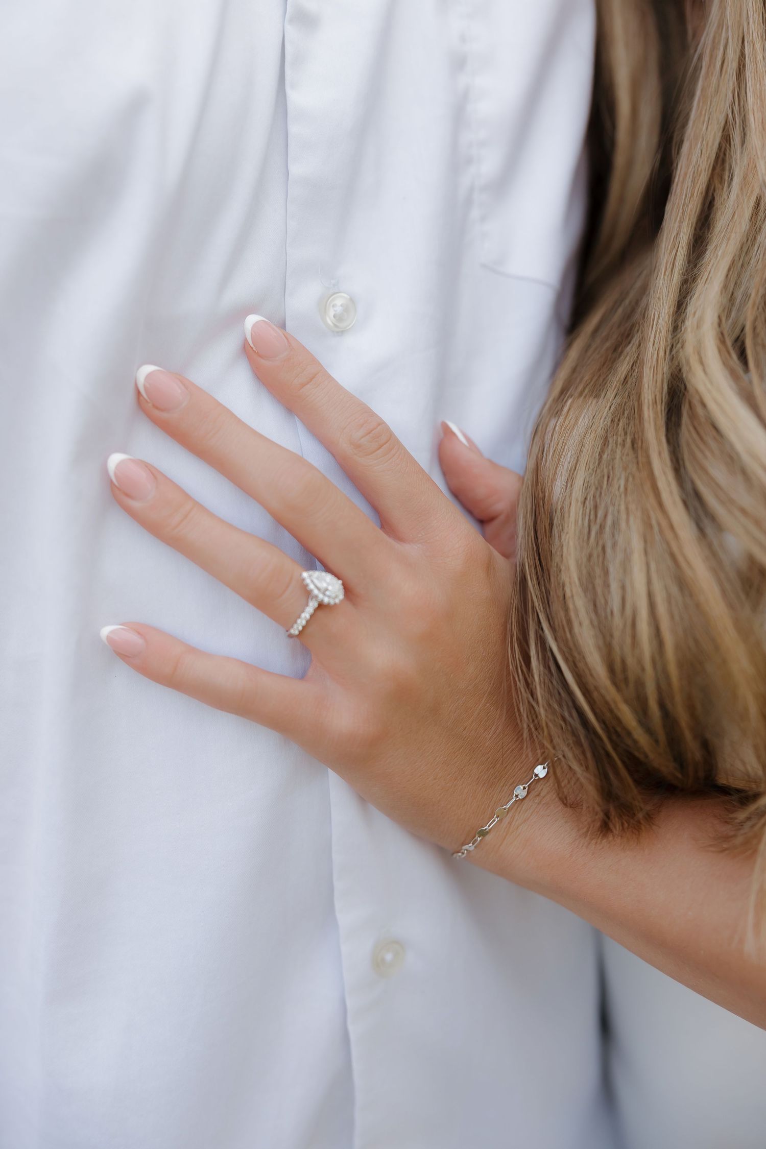 Close up of a hand wearing a sparkling diamond engagement ring against a white fabric background.