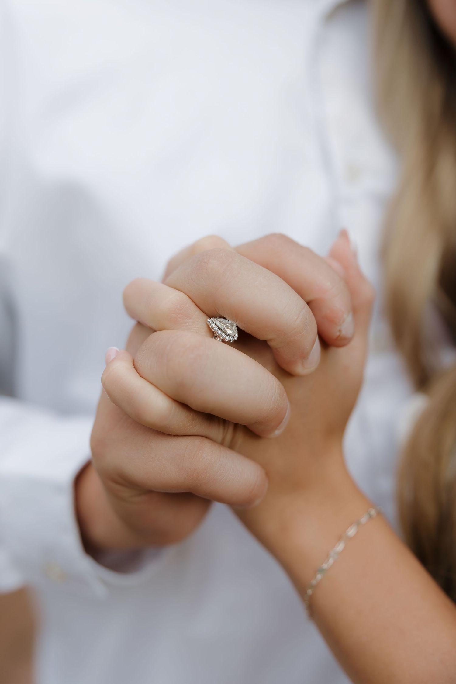 Close-up of hands clasped together showing an elegant diamond engagement ring and delicate bracelet.