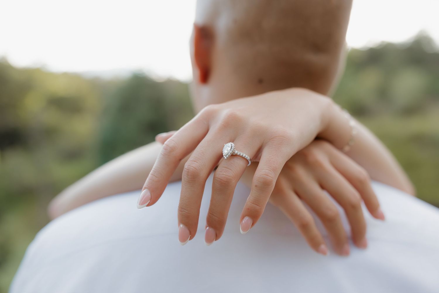 Hands with engagement ring shown in various close-up poses against a blurred outdoor background.