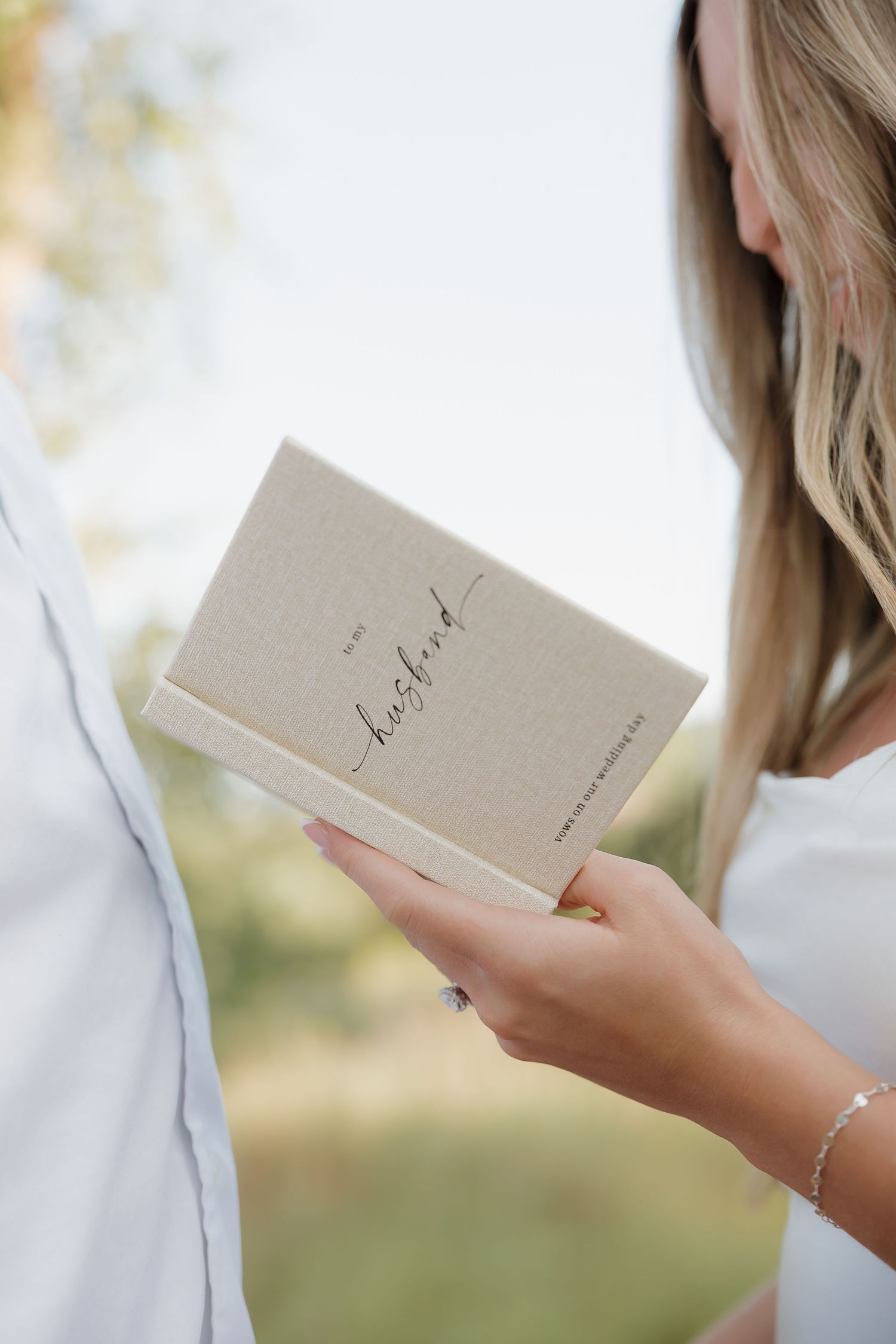 Close-up view of hands holding a beige paper card or note in an outdoor setting.