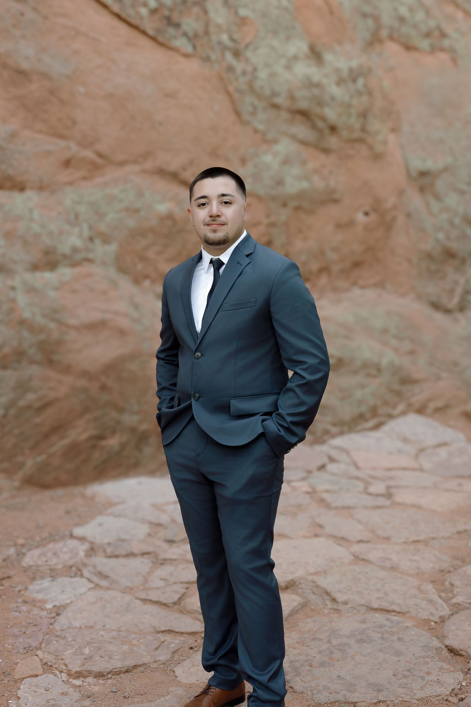 Groomsmen in dark suits pose on red rock formations during an outdoor wedding photoshoot.