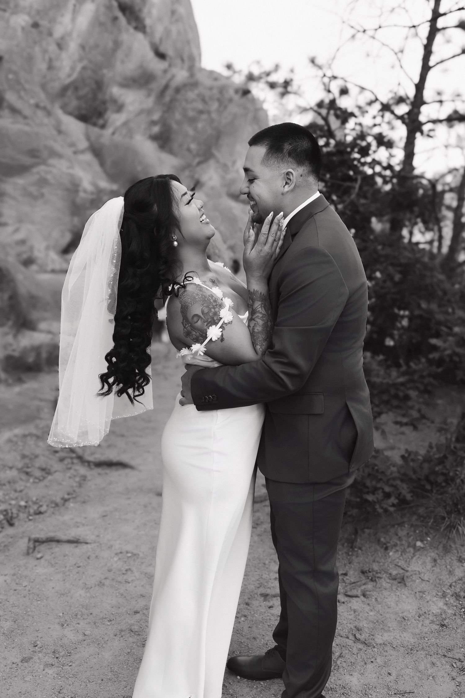 A black and white wedding portrait showing a tender moment between newlyweds against a rocky outdoor backdrop.