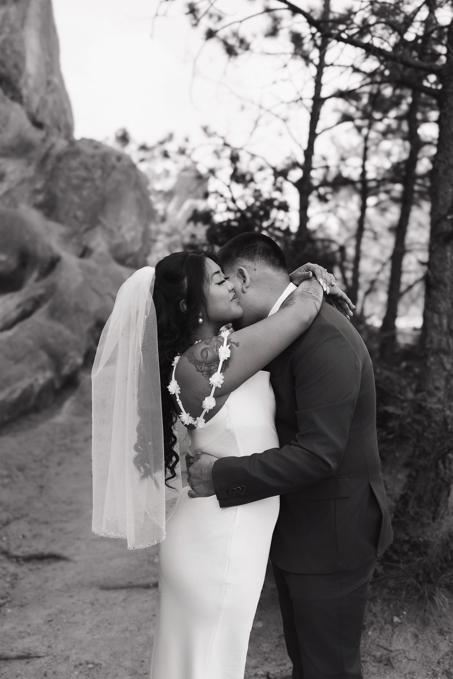 An intimate black and white wedding photograph capturing a kiss between newlyweds near dramatic rock formations.